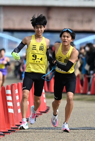 男子・三田市の４区山本侑輝選手（左）からたすきを受ける５区久山大祐選手＝加古川市の加古川河川敷マラソンコース（撮影・風斗雅博）