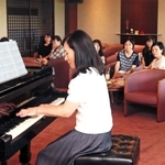 順番にグランドピアノを弾くメンバー＝三田市武庫が丘７、三田屋本店