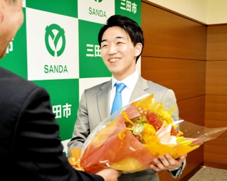 田村克也市長から五段昇段を祝う花束を受け取り、笑顔を見せる冨田誠也さん（右）＝三田市役所