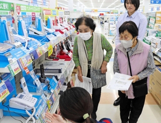 三田署員（右奧）に付き添われ、電器店で電話機を選ぶ利用者＝三田市けやき台１