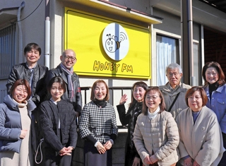看板の前に集合したハニーＦＭの門垣登志子代表（中央）やかつてのスタッフら＝三田市高次１