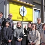 看板の前に集合したハニーＦＭの門垣登志子代表（中央）やかつてのスタッフら＝三田市高次１
