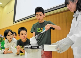 有馬高校の生徒から指導を受け、液体窒素に入れた木の葉を慎重に取り出す子どもたち＝三田市駅前町
