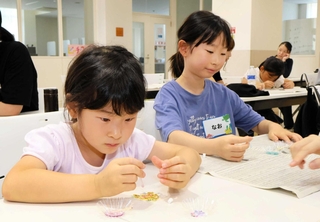 砂浜に落ちていたプラスチックごみなどを使い、キーホルダーを作る子どもたち＝三田市学園上ケ原