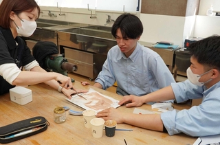 愛和義肢製作所の義肢装具士（左）に教わりながら、肌の色を再現する学生ら＝三田市福島