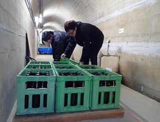 ダム内部の通路に地酒を並べる酒蔵の関係者たち＝三田市加茂（宝塚土木事務所提供）