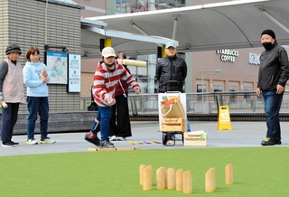 モルックを投げる菖蒲十馬さん（左から３人目）。地域住民との輪も自然と広がる＝三田市駅前町