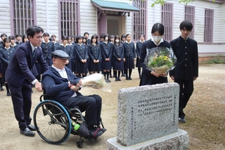 顕彰碑に花を手向けた吹奏楽部員と、犠牲になった石井勝さんの兄の努さん＝三田市南が丘２