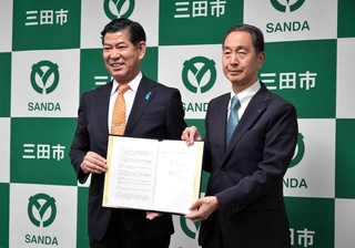 協定書を手にする田村克也市長（左）と阪急交通社の山川豊治社長＝三田市役所
