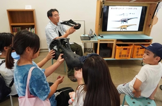 「研究員トーク」で、子どもたちに恐竜の模型を使いながら説明する田中公教研究員＝三田市弥生が丘６