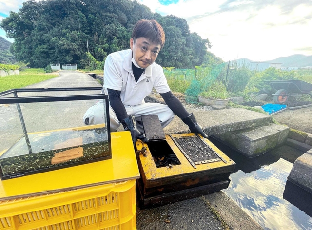 捕まえた山本英雄さん。ウナギ釣りが趣味で、手にしているいけすに入れて用水路で飼っている＝たつの市揖保川町袋尻
