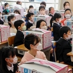 市から贈られた学用品の箱の前に座る新１年生と付き添いの保護者＝龍野小学校