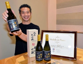 フランスの品評会でプラチナ賞に輝いた日本酒「播州一献　純米大吟醸　山田錦」を掲げる壺阪専務＝山陽盃酒造