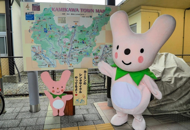 大型観光案内板の前でハートのまちをアピールする「カーミン」＝神河町鍛治