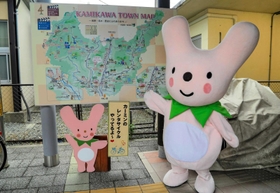 大型観光案内板の前でハートのまちをアピールする「カーミン」＝神河町鍛治