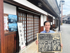 旧店舗時代の店構えを描いた版画家・乾太さんの作品を持つ小林實さん＝たつの市龍野町下川原