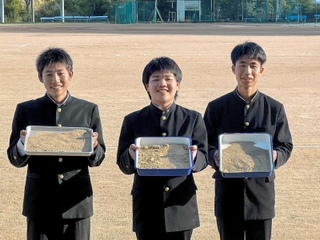 約６兆４６００億個の砂粒があるとされるグラウンドの前に立つ（左から）川中大雅さん、陸井陽登さん、宮下裕生さん＝相生高校