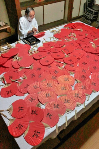 魔よけを意味する赤のうちわに宮司が文字を入れていく＝赤穂市坂越