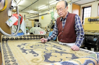 赤穂緞通の染み抜きで、表面の状態を確認する田川芳弘さん＝赤穂市坂越