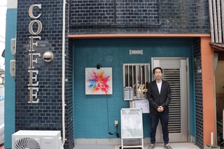 壁面の「ＣＯＦＦＥＥ」の文字が目印。店の前に立つ店長の田村寿之さん＝コーヒーロースターズハブ