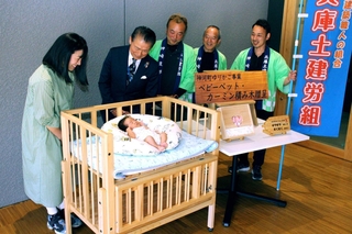 町からベビーベッドの贈呈を受けた小林采生ちゃん（手前）と母美結さん（左）＝神河町粟賀町