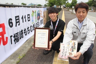 制定を祝う横断幕の前で町産もち麦をＰＲする「もちむぎのやかた」の松井永敏代表（右）と福崎町職員の河本直也さん＝福崎町西田原