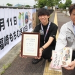 制定を祝う横断幕の前で町産もち麦をＰＲする「もちむぎのやかた」の松井永敏代表（右）と福崎町職員の河本直也さん＝福崎町西田原