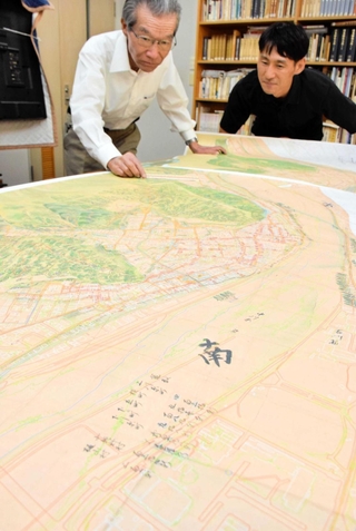池田善考さん（左）が製作した重ね図。たつの市役所などがある地域（絵図の手前）が、江戸期は揖保川だったことが分かる＝たつの市龍野町上霞城