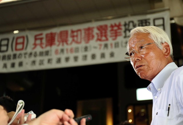 「５選当確」の報を受け、事務所前で報道各社の取材に応じる井戸敏三氏。多選の弊害を問う質問に険しい表情を見せる＝２日夜、神戸市中央区（撮影・大山伸一郎）
