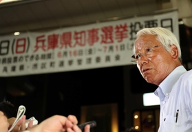 「５選当確」の報を受け、事務所前で報道各社の取材に応じる井戸敏三氏。多選の弊害を問う質問に険しい表情を見せる＝２日夜、神戸市中央区（撮影・大山伸一郎）