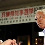 「５選当確」の報を受け、事務所前で報道各社の取材に応じる井戸敏三氏。多選の弊害を問う質問に険しい表情を見せる＝２日夜、神戸市中央区（撮影・大山伸一郎）