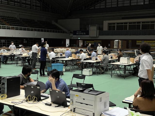 照明が半分落ち、薄暗くなった開票所で票を再集計する職員ら。空調も切れ、扇子であおぐ姿も見られた＝１９日午前１時３６分、西宮市立中央体育館