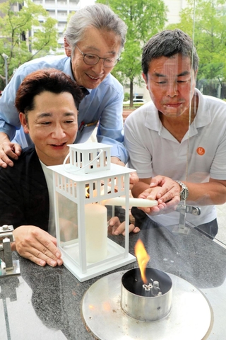 豪雨で被災した広島県坂町に届けようと、「１・１７希望の灯り」から分灯するＨＡＮＤＳ代表理事の藤本真一さん（左手前）らメンバー＝神戸市中央区加納町６
