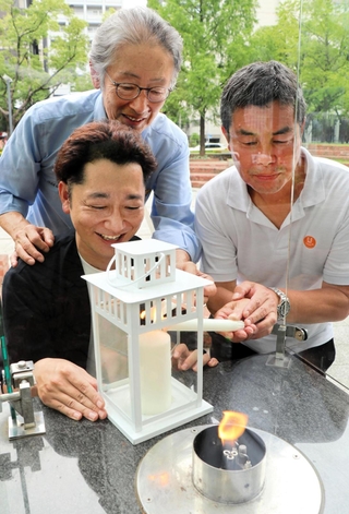 豪雨で被災した広島県坂町に届けようと、「１・１７希望の灯り」から分灯するＨＡＮＤＳ代表理事の藤本真一さん（左手前）らメンバー＝神戸市中央区加納町６