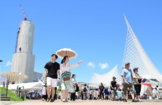 厳しい暑さに見舞われた神戸市内。青空の下、日傘やうちわを手にイベント会場を行き交う人ら＝１６日午後、同市中央区波止場、メリケンパーク（撮影・中西幸大）