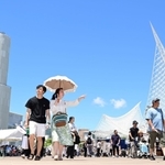 厳しい暑さに見舞われた神戸市内。青空の下、日傘やうちわを手にイベント会場を行き交う人ら＝１６日午後、同市中央区波止場、メリケンパーク（撮影・中西幸大）