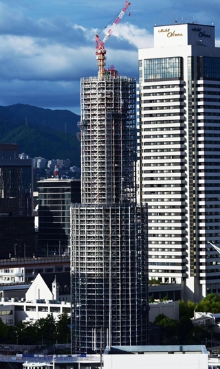 工事用のシートが外され、鉄骨の足場が西日を受けて輝く神戸ポートタワー＝７日午後、神戸市中央区東川崎町１から波止場町方面を望む