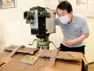 関東大震災の撮影に使われたとみられるカメラを手にする安井喜雄館長＝神戸映画資料館