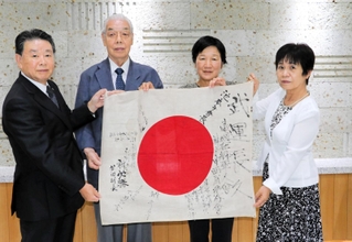 「キセキ遺留品返還プロジェクト」のスタッフ（右から２人目）から、日の丸を手渡された北井和夫会長（同３人目）＝神戸市長田区西尻池町２