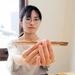 パレスチナのオリーブの木で作られた箸を手にする高橋智恵さん。木目が温かい＝川西市内