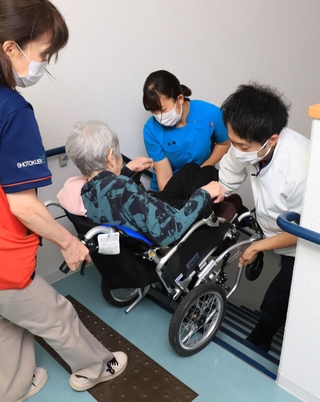 車いすの利用者を階段で４階へ運ぶ高校生（中央）と職員＝西宮市今津港町（撮影・吉田敦史）