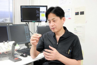 「重症患者は、激しい運動などを控え、無理をしないことが大切」などと話す当麻正直医師。手にするのはＴＡＶＩで使う人工弁＝尼崎市東難波町２、兵庫県立尼崎総合医療センター