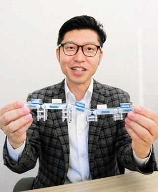 ベルトコンベヤーのカプセルトイを掲げるオークラ輸送機の金川健太朗さん＝加古川市野口町古大内