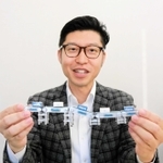 ベルトコンベヤーのカプセルトイを掲げるオークラ輸送機の金川健太朗さん＝加古川市野口町古大内