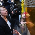 伯母といとこの名前が入った銘板を取り付け、手を合わせる鶴崎光英さん＝１７日午後、神戸市中央区加納町６、東遊園地（代表撮影）