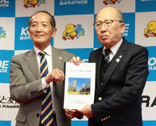 神戸マラソン実行委員会の松本俊裕会長（右）に提言書を手渡す将来構想検討委員会の山口泰雄委員長＝２３日午後、兵庫県民会館