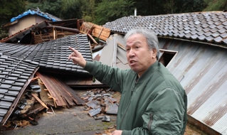阪神・淡路大震災で父の一男さんを亡くした惣田亜喜夫さん。能登半島地震では思い出の詰まった実家（後方）が全壊した＝石川県珠洲市正院町平床（撮影・笠原次郎）