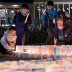 灯籠にろうそくで火をともす子どもら＝１６日午後６時３２分、神戸市中央区加納町６、東遊園地（撮影・斎藤雅志）