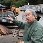 阪神・淡路大震災で父の一男さんを亡くした惣田亜喜夫さん。能登半島地震では思い出の詰まった実家（後方）が全壊した＝石川県珠洲市正院町平床（撮影・笠原次郎）