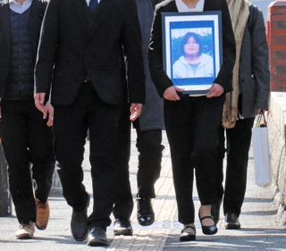 提訴にあたり、岡田幸子さんの遺影を手に神戸地裁に入る遺族（前列２人）や弁護士たち＝神戸市中央区橘通２、神戸地裁